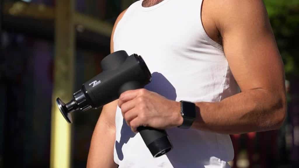 A man with a beard and a white T-shirt is holding a massage gun
