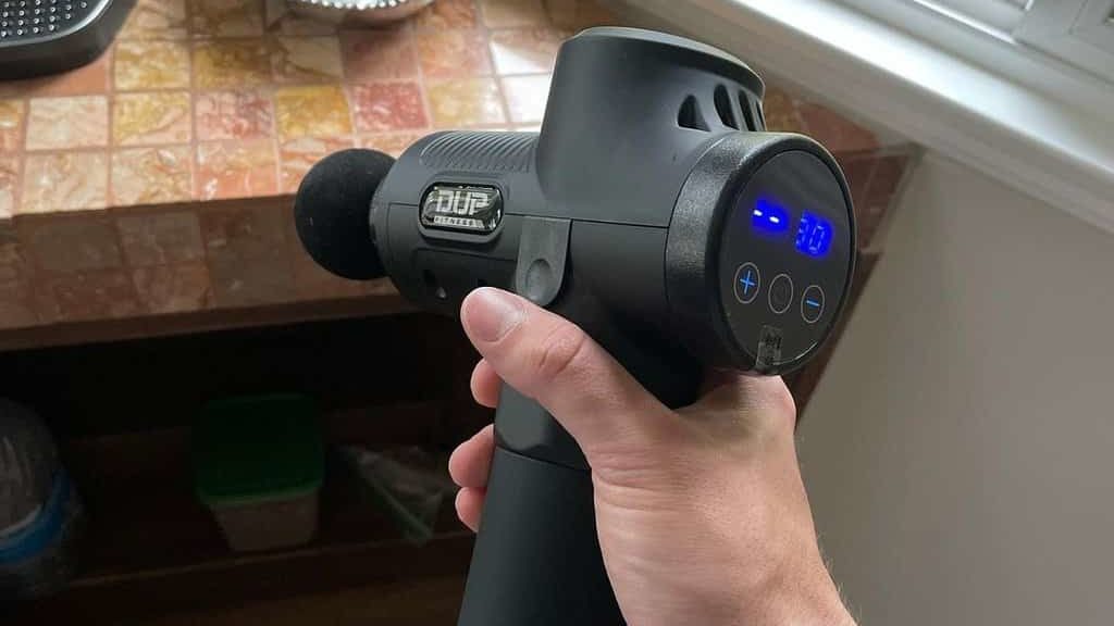 black massage gun in hand against the background of the table