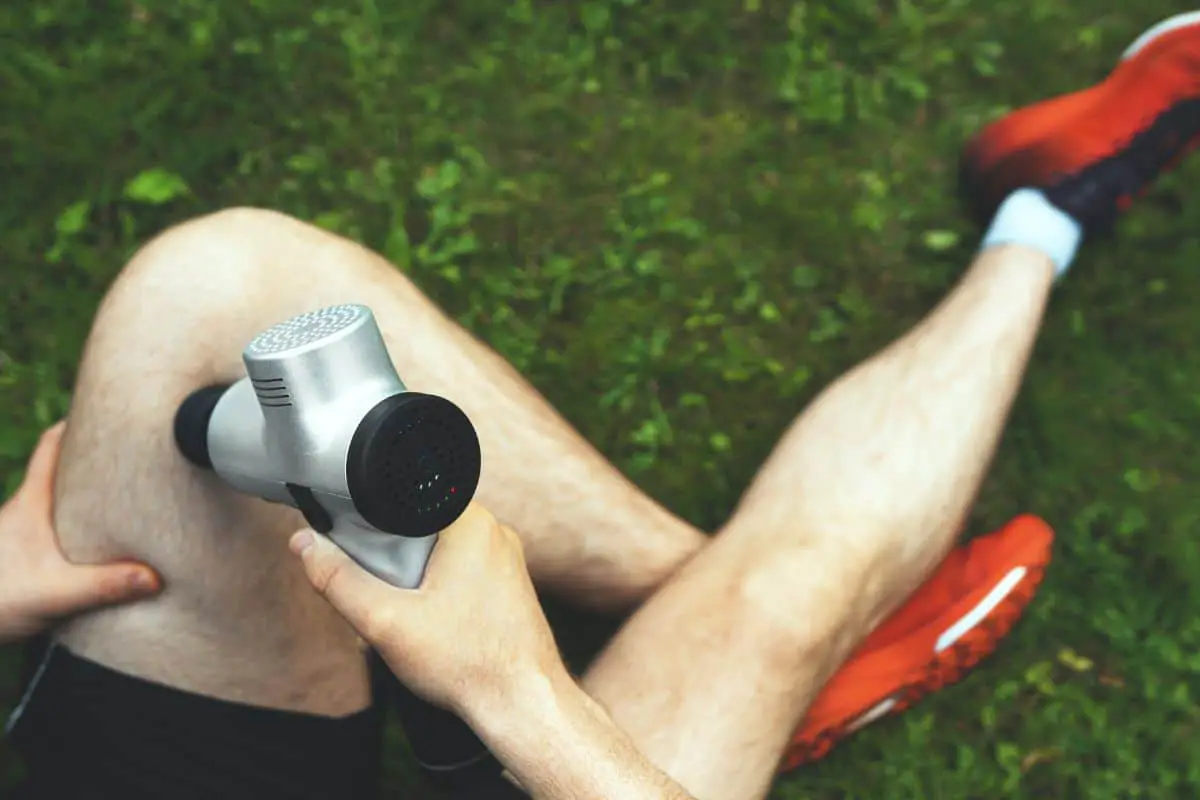 athlete massaging his feet with a percussion massager 