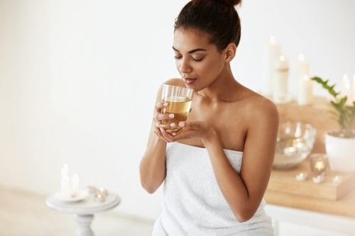 African girl drinking water resting in spa salon. Closed eyes.