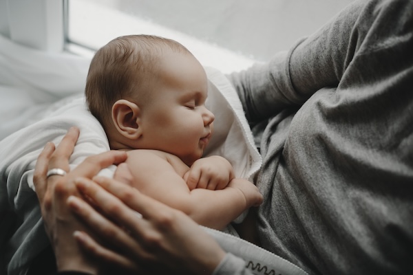 parent-comforting-newborn-after-baby-massage Parent gently holding and comforting a sleeping newborn baby.