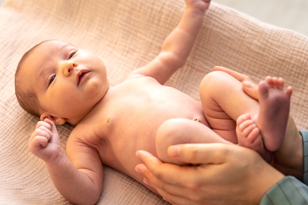 knees-to-tummy-baby-gas-relief Parent gently bringing a baby’s knees towards their tummy during a gas-relief massage.