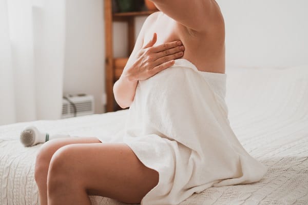 Young woman examines her breasts and lymph nodes with her hands while sitting at home in the bedroom
