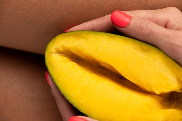 Symbolic representation of labia massage and female anatomy using a sliced mango to illustrate body awareness and self-care.