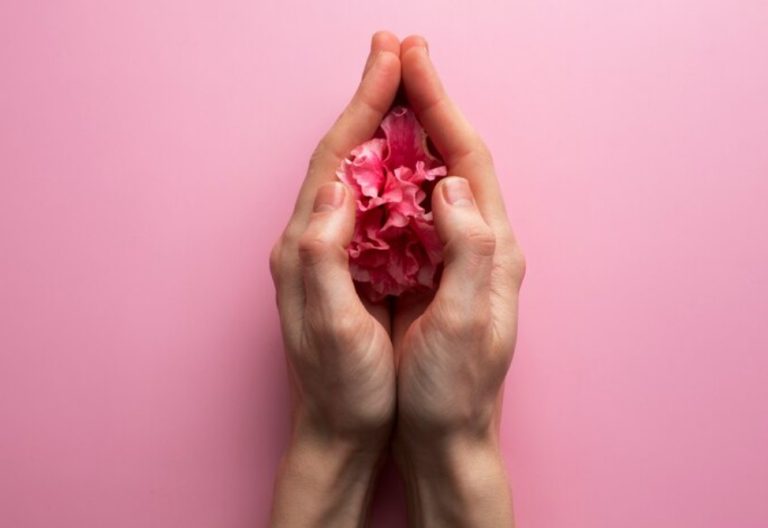 Cupped hands holding pink flower petals against a pink background