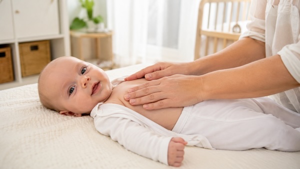 Parent gently resting both hands on a calm baby’s upper chest while demonstrating how to massage a baby with a cough.