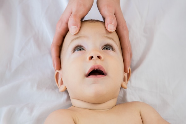 Parent gently holding and massaging a baby’s head while the baby lies on a soft surface.