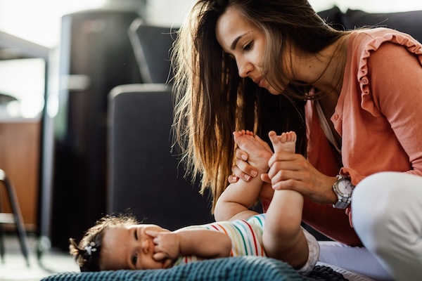 Parent gently massaging a baby’s legs while the baby lies on a soft mat.